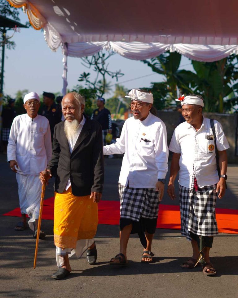 Putu Gangga walking alongside Balinese community elders during a traditional temple ceremony